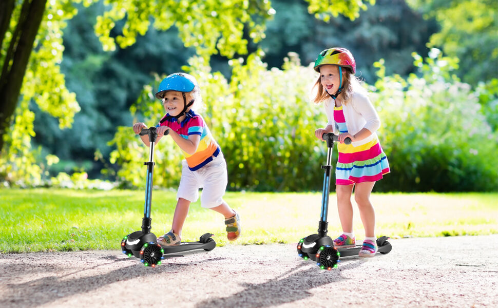 Two children in helmets riding GRAFLO three-wheel scooters together in a park