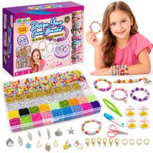 A girl holding a finished beaded bracelet beside the GRAFLO Design Your Own Bracelet box, with the 14,000 bead tray, charms, clasps, jump rings, elastic cords, scissors and tweezers laid out