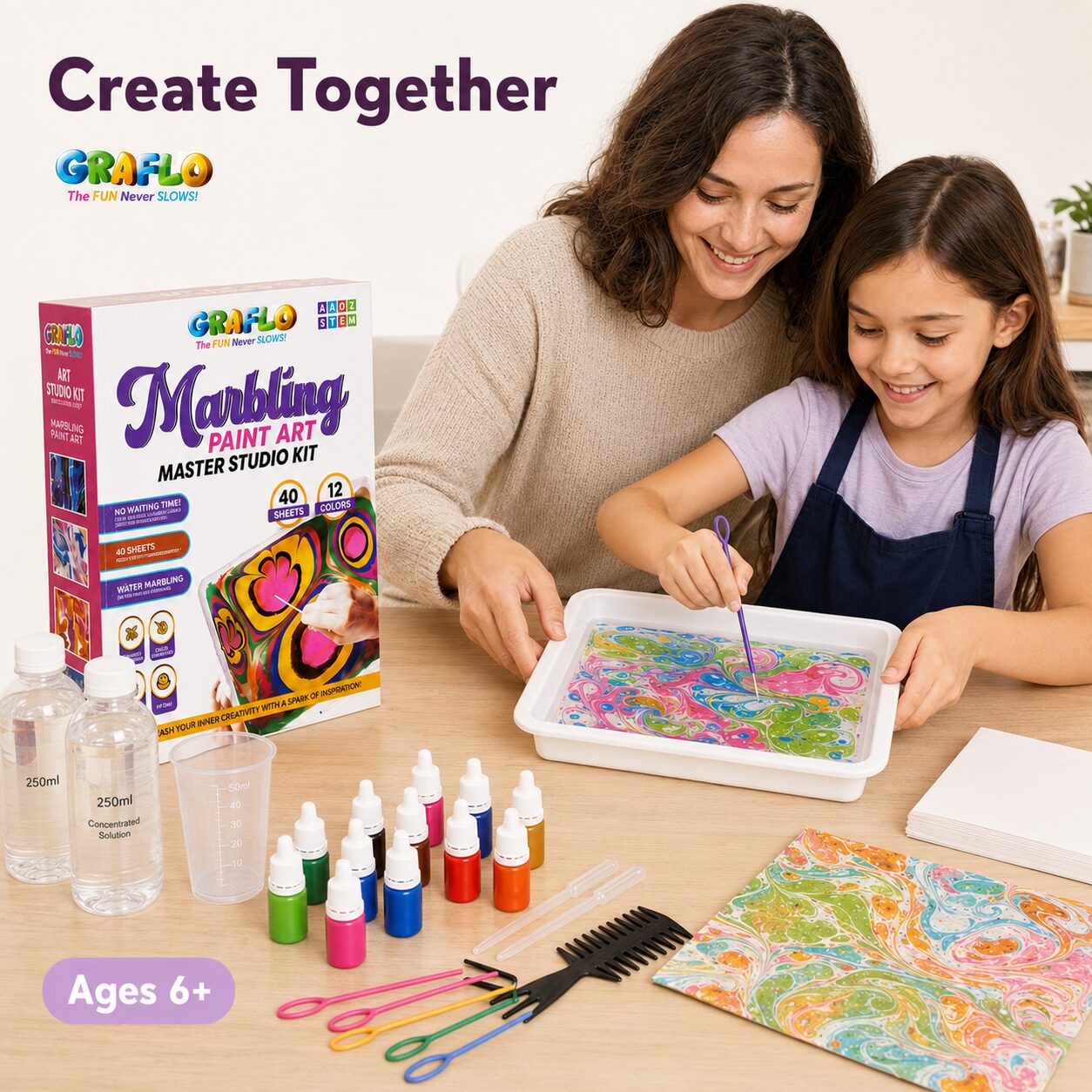 A mother and daughter marbling a print together at a table with the GRAFLO kit laid out, labelled ages 6 and up
