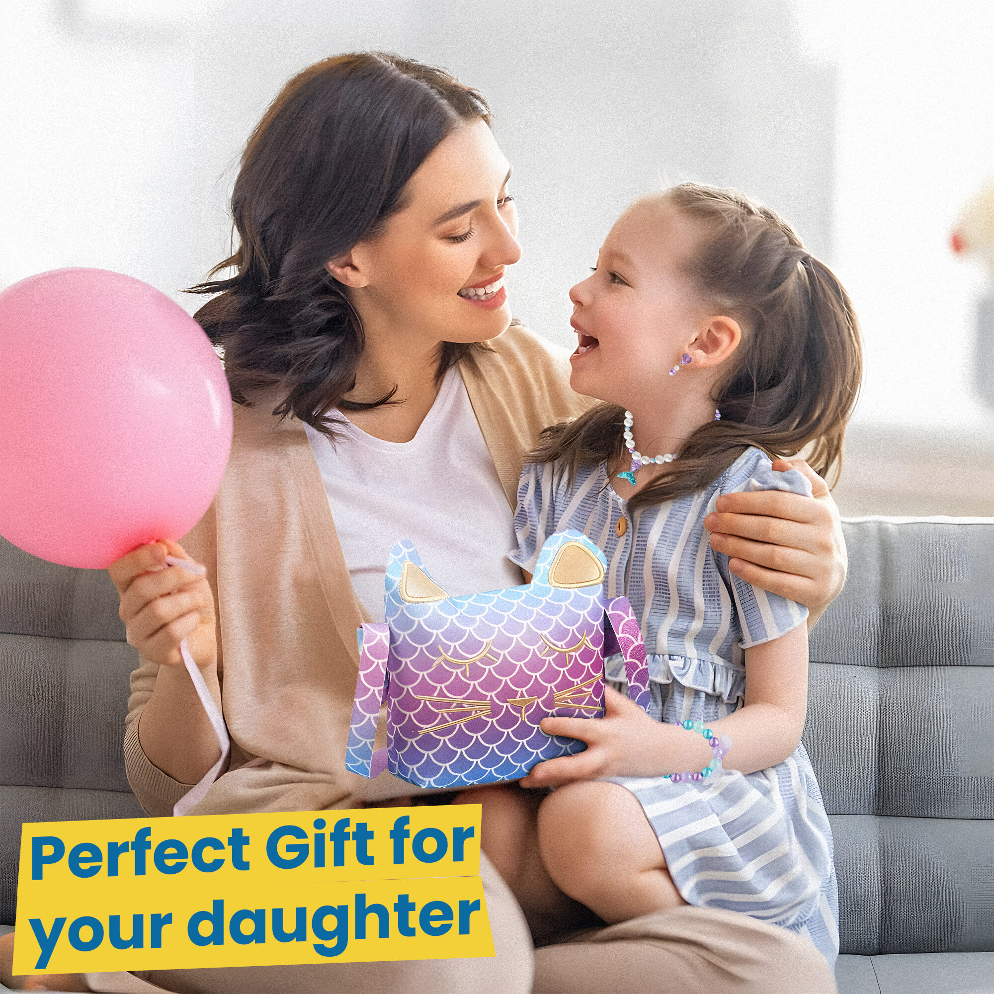 A mother and daughter on a sofa with a pink balloon, the daughter holding the mermaid cat purse - a gift for your daughter